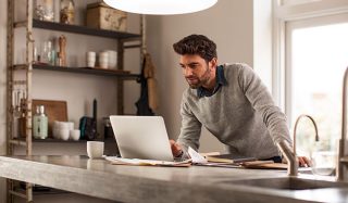 Hombre utilizando un portátil en una oficina doméstica bien iluminada con iluminación LED para una configuración eficiente del trabajo a distancia.